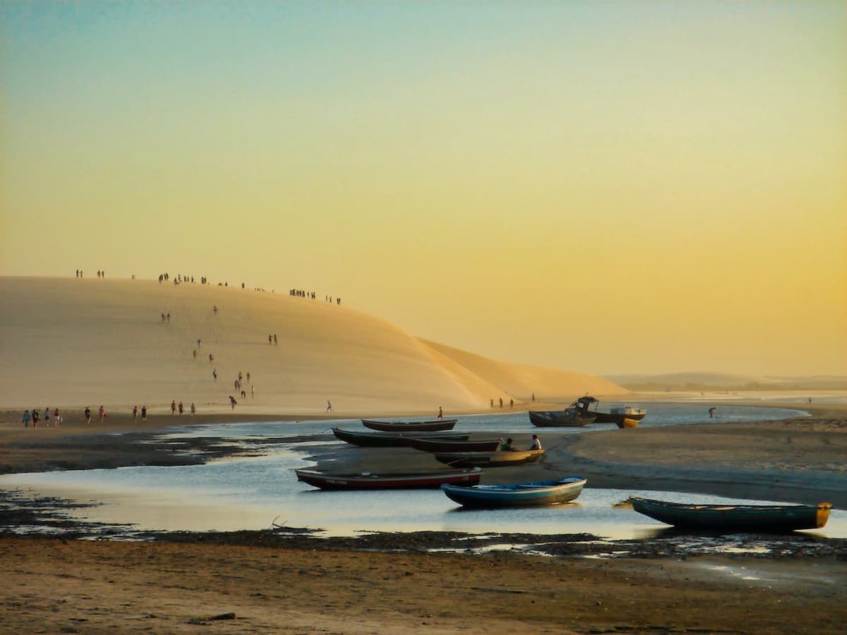 Imagem de um pôr de sol com dunas no fundo, e barcos na água