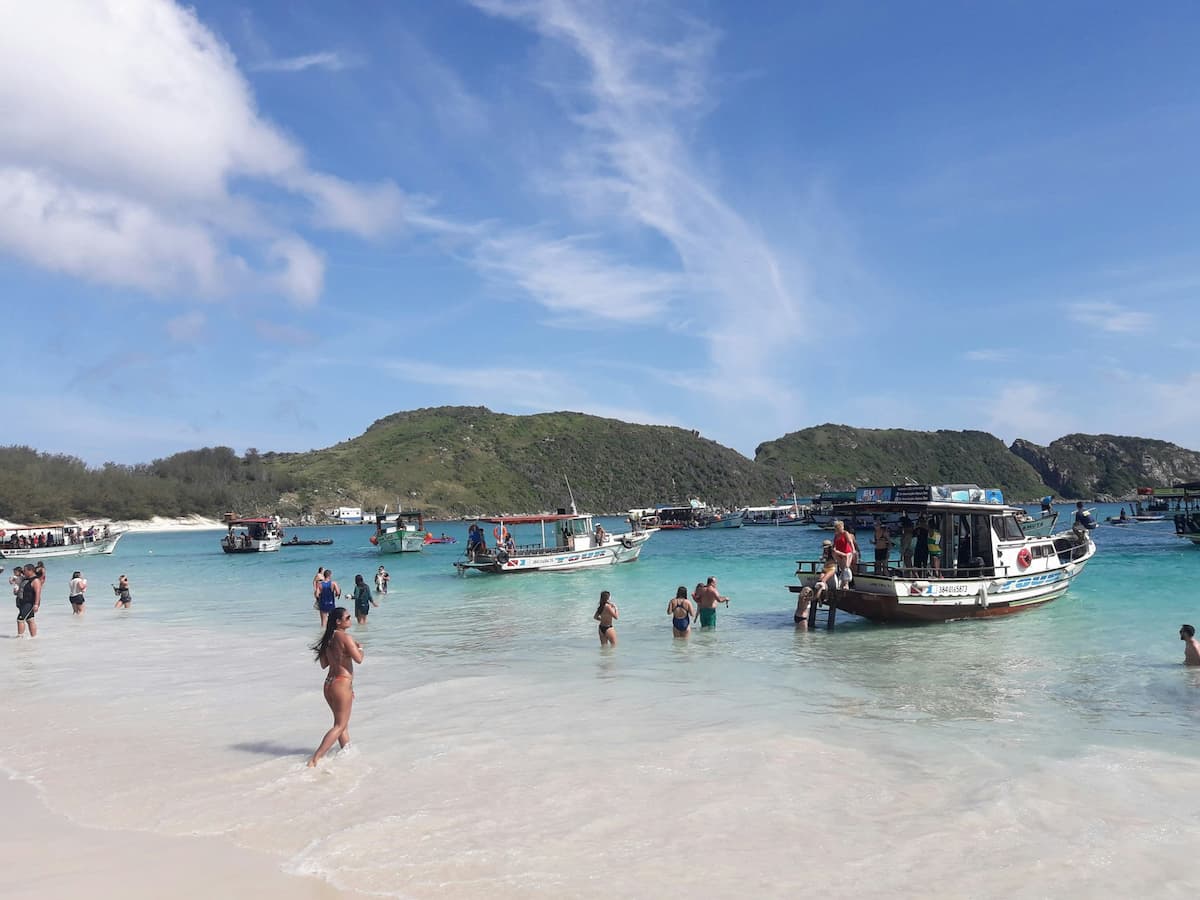 Imagem de uma praia com pessoas e um barco na água