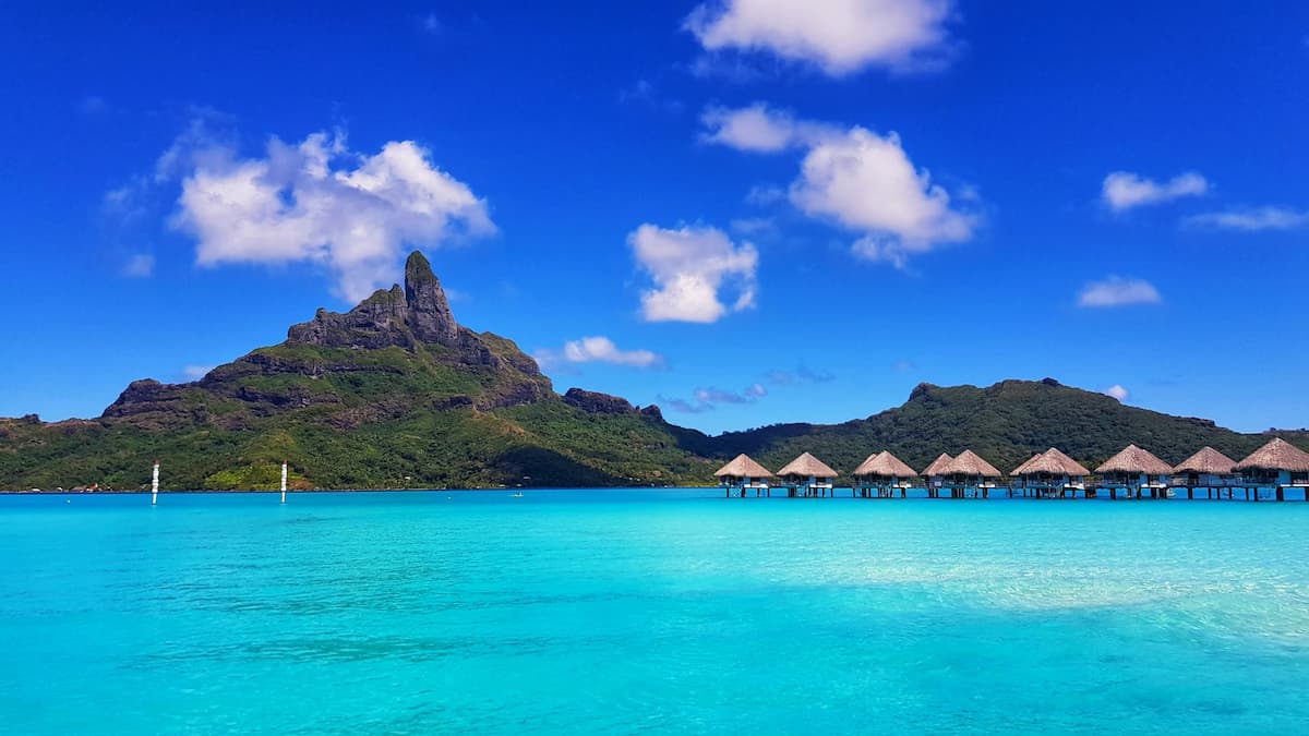 Imagem de uma praia em um dia de sol com uma montanha no fundo