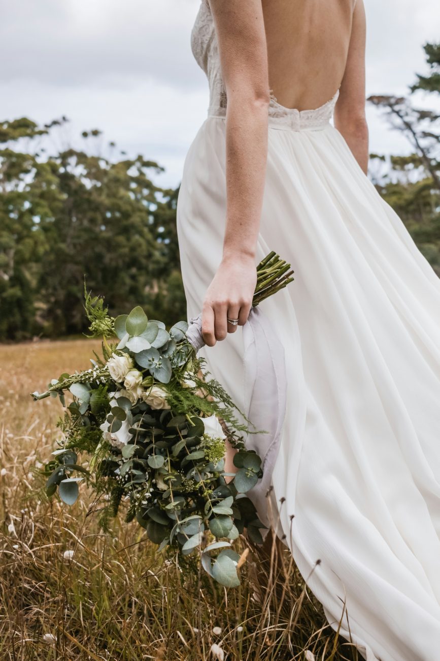 noiva segurando buquê de flores e caminhando pelo campo