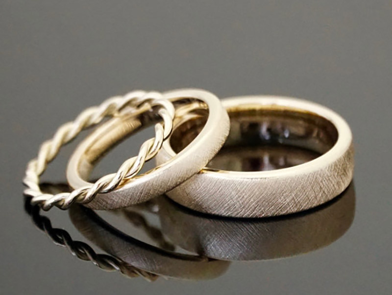 Três tipos de aliança de casamento. Dois em aço escovado e um em ouro trançado.