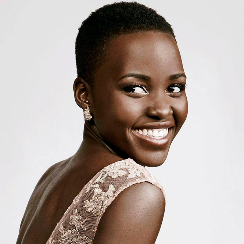 Mulher negra de costas, com a cabeça levemente virada para a direita, enquanto sorri.