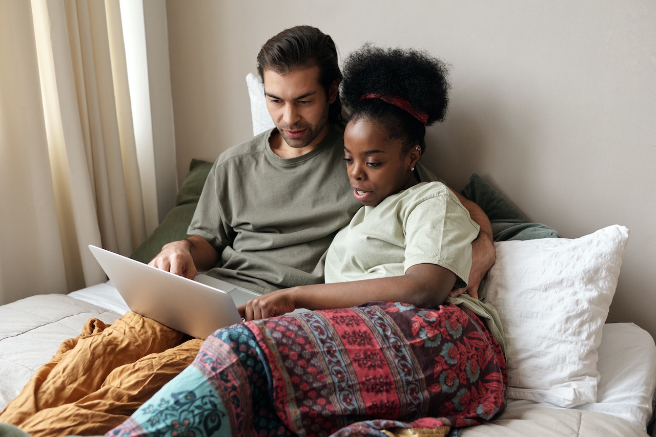 Casal abraçado em uma cama olhando para um computador