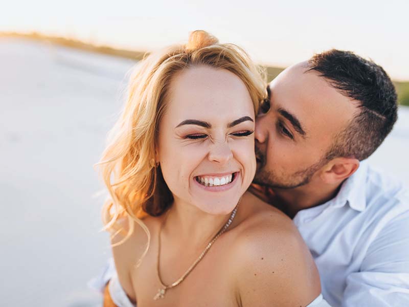A bearded man and a blond woman hugging against the background of white sand. Portrait of emotional people at sunset. Love in the desert newlyweds. The love story of merry lovers young.Kiss and smile.