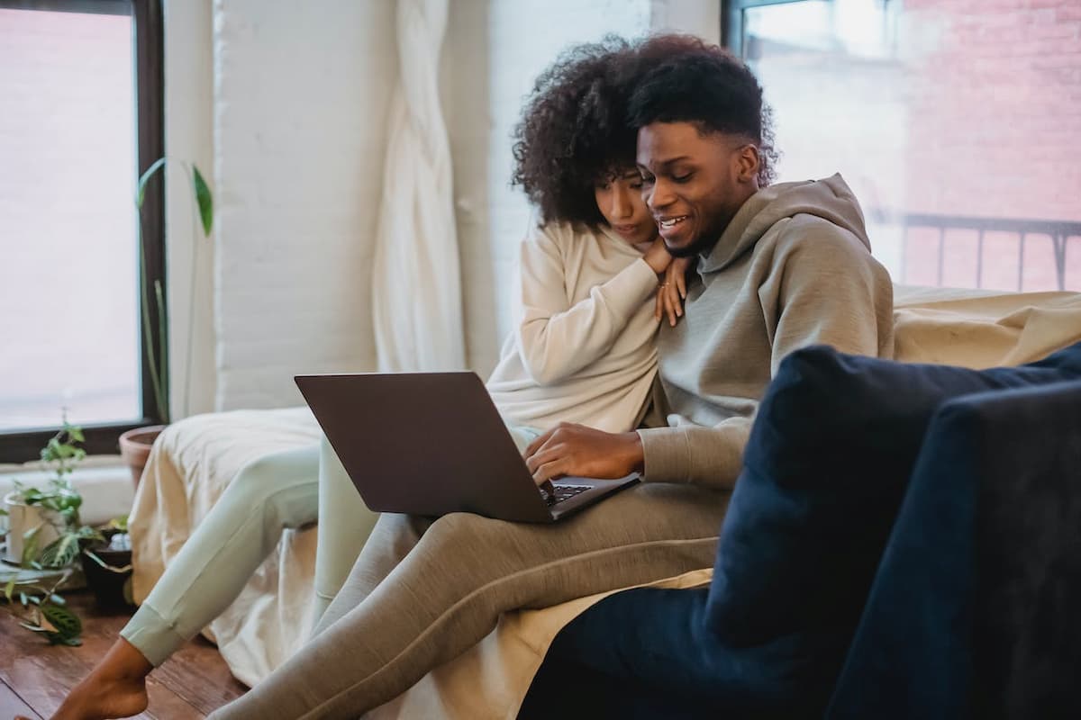 Imagem d eum casal sentado no sofá vendo o computador abraçados