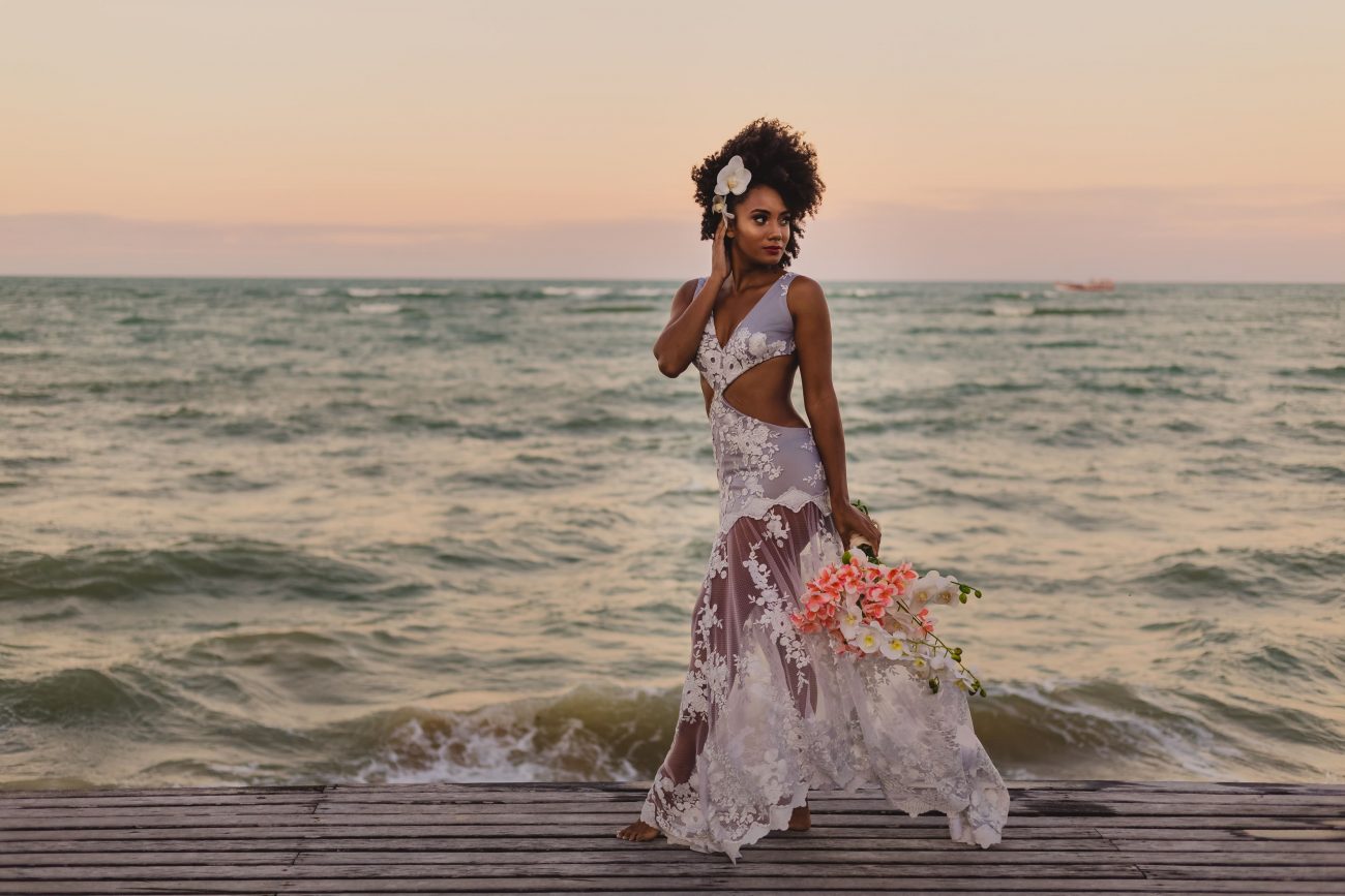 Noiva faz um ensaio fotográfico dentro do mar, ela segura um buquê de rosas e um pente no cabelo.