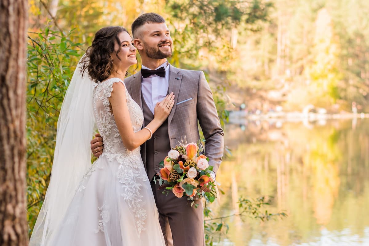 Mulher de cabelo curto com vestido de casamento e homem com terno cinza em uma paisagem com árvores