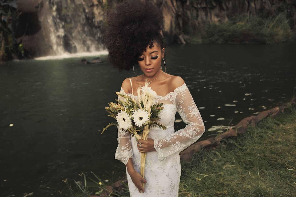 Mulher vestida de noiva segurando flores na frente de lago