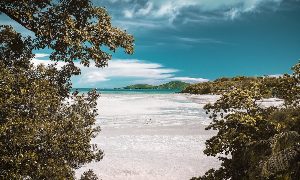 Imagem da praia com areia branca e o mar ao fundo durante o dia