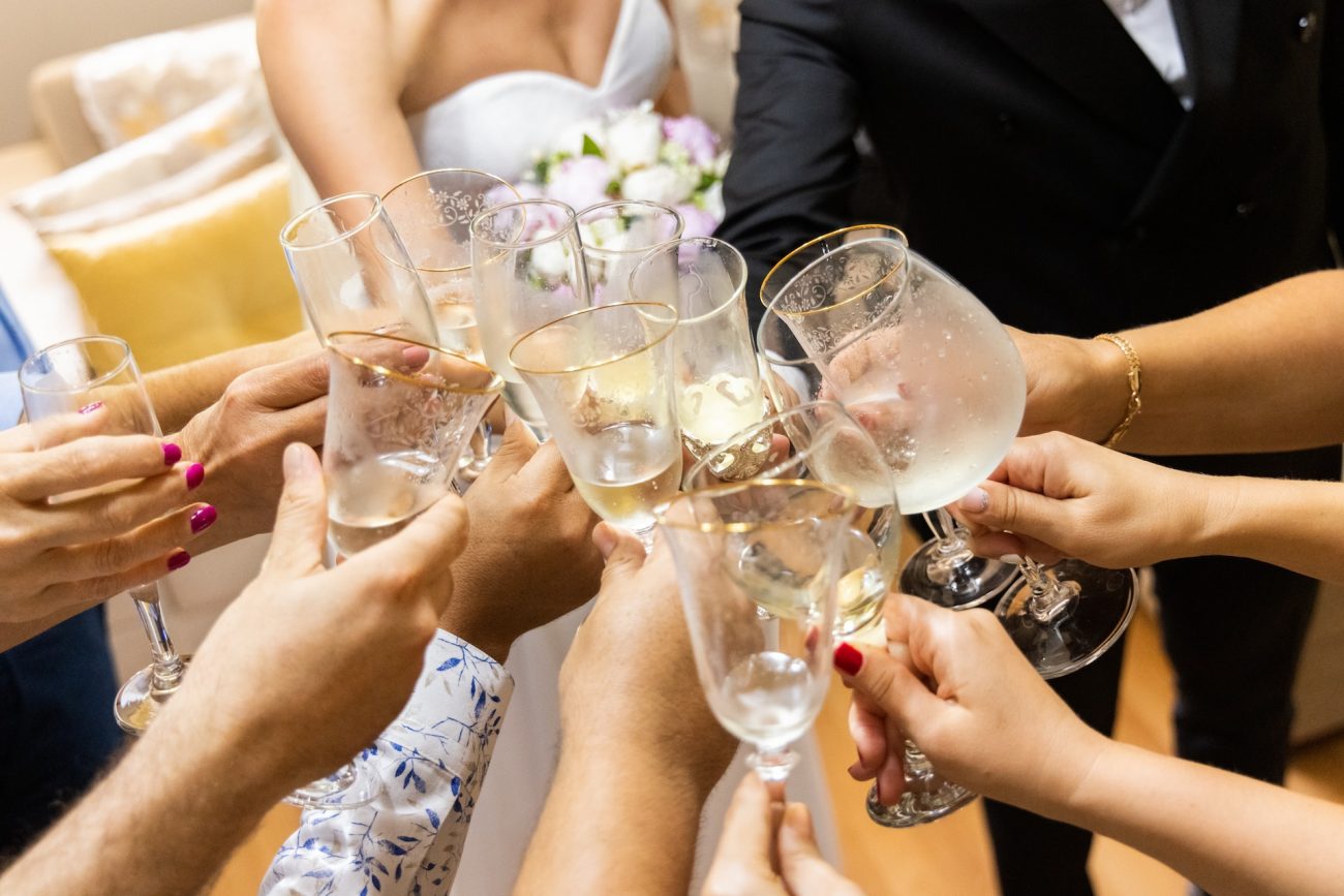 Mulher de vestido de noiva branco brindando com seus convidados segurando taças
