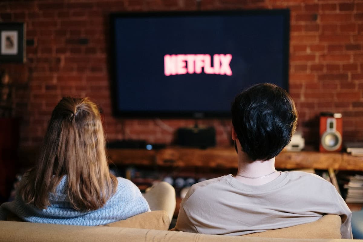 Imagem de um casal sentados no sofá assistindo televisão
