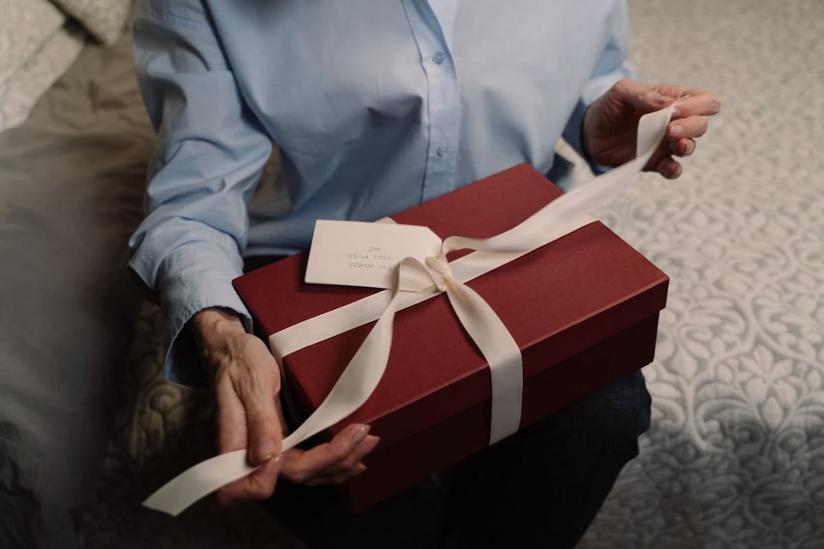 Imagem de uma pessoa com blusa azul segurando um presente com papel vermelho e laço branco
