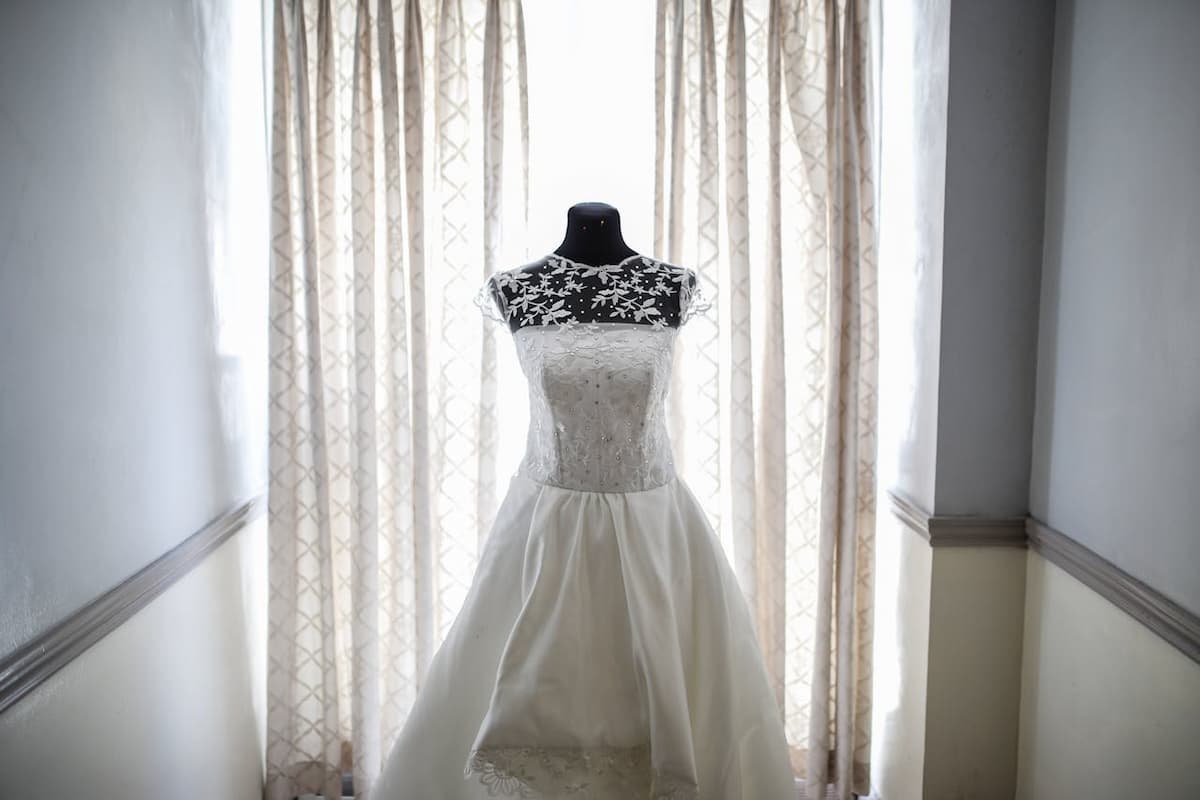 Imagem de um vestido de noiva no manequim na janela|||||||||||Imagem das costas de um vestido de noiva sendo abraçada pelo noivo|Imagem de uma noiva segurando o buquê em um jardim|Imagem de uma noiva na frente de um lugar com grandes portas fechadas