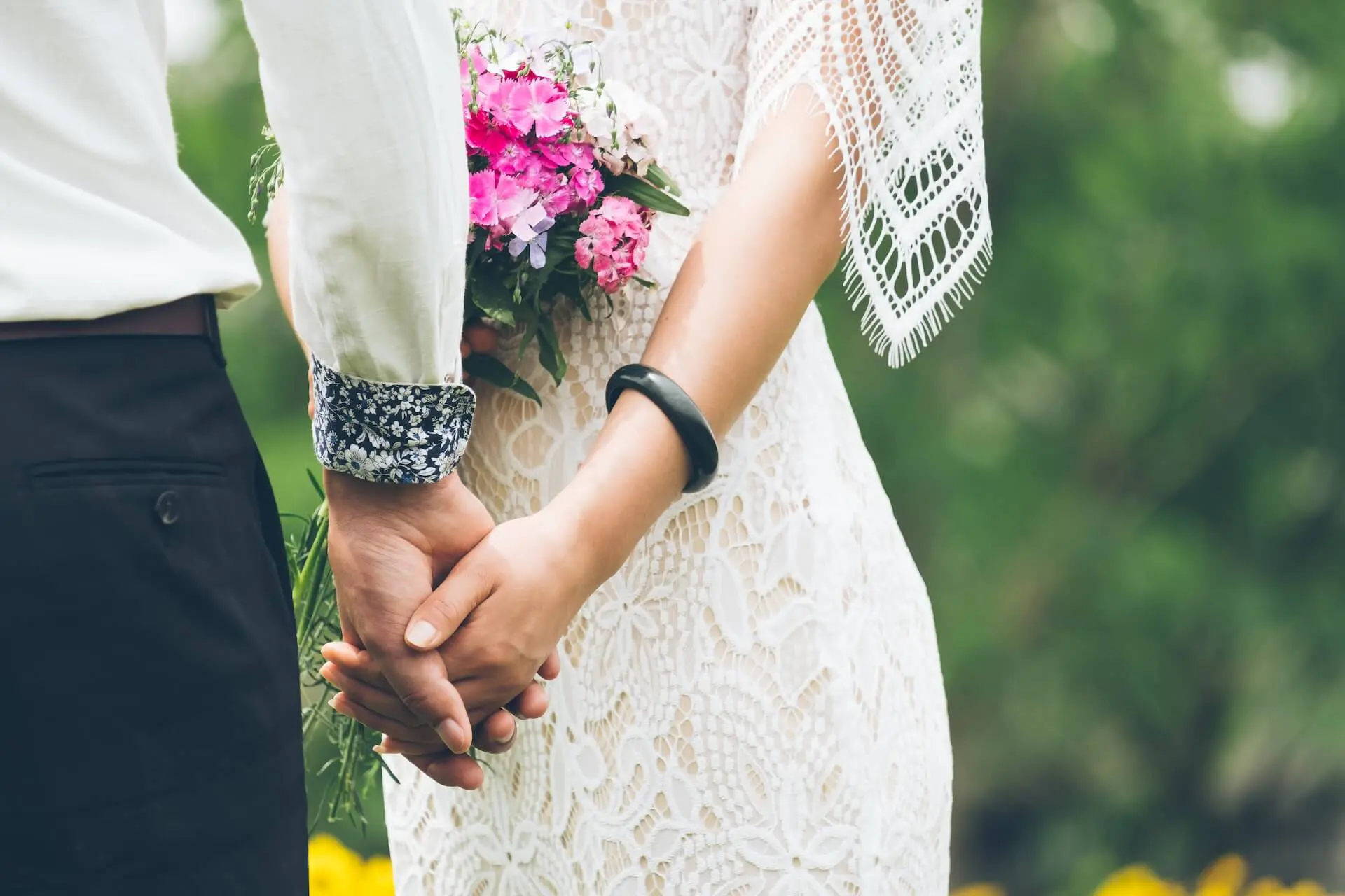 noiva e noivo de mãos dadas com um buquê de rosas entre eles