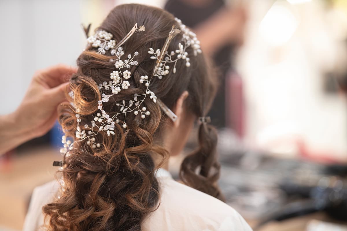 Mulher se arrumando com acessórios florais em seu cabelo|rabo-de-cavalo-é-um-dos-tipos-de-penteados-para-noiva|coque-clássico-para-noivas|trança-entre-os-tipos-de-penteados-para-noivas|cabelo-semi-preso-para-noiva|coque-messy-para-noivas|tipos-de-penteados-rabo-de-cavalo|penteado-lateral-para-noivas|coque-baixo-para-noivas|tipos-de-penteados-para-noivas|tipos-de-penteados|tipos de penteados||Mulher de cabelo curto com vestido de casamento e homem com terno cinza em uma paisagem com árvores|Mulher vestida de noiva em uma montanha segundo a mão de uma pessoa|Noivos sentados no cais|Mulher vestida de noiva segurando o buquê em uma praça|Mulher de vestido de noiva olhando pela janela|Mulher vestida de noiva segurando flores na frente de lago|Homem e mulher vestidos de noivos andando em uma floresta|Ensaio de noivos em um campo|Homem de terno azul com mulher de vestido de noiva|Mulher vestida de noiva abraçando homem durante o dia|Noiva em seu casamento durante o dia