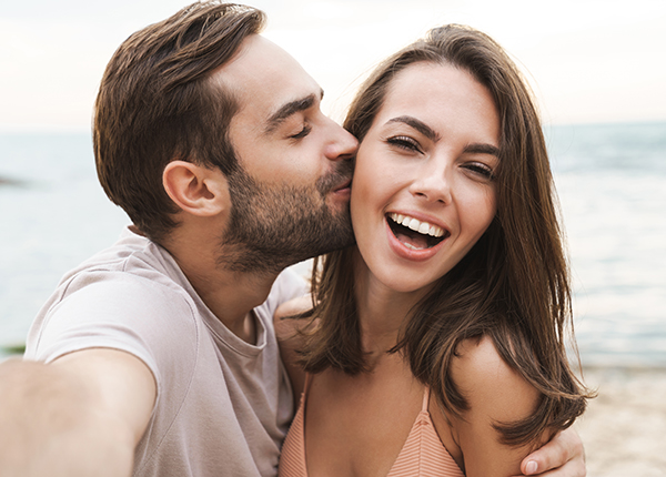 |Image of young happy man kissing and hugging beautiful woman while taking selfie photo on sunny beach|A guy carrying a girl on his back