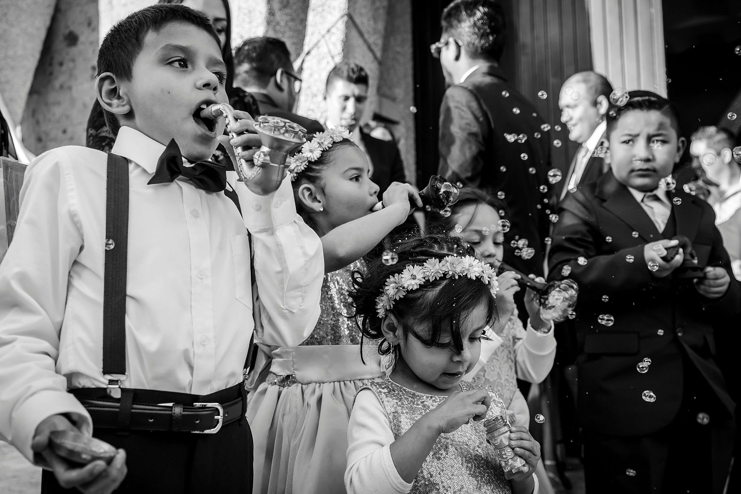 Daminhas e pajens brincam com bolhas de sabão na saída de um casamento. Cena espontânea em preto e branco.|daminhas e pajen|daminhas e pajen|daminhas e pajen|daminhas e pajen|||Meninas vestidas de daminhas de casamento.|Daminha e pajem em cerimônia ao ar livre. O menino sorri