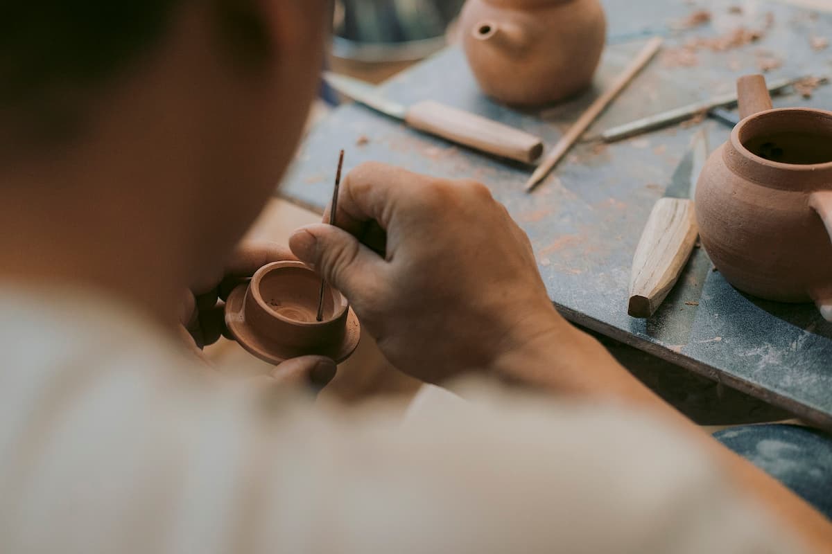 Imagem de uma pessoa pintando na cerâmica|Imagem de dois vasos de cerâmica|Imagem de uma tigela de cerâmica sendo feita|Imagem de um passeio de balão no ar em um lugar ao ar livre|Imagem de uma televisão em um ambiente escuro|Imagem de dois quadros com frases na parede|Imagem de ferramentas de jardinagem