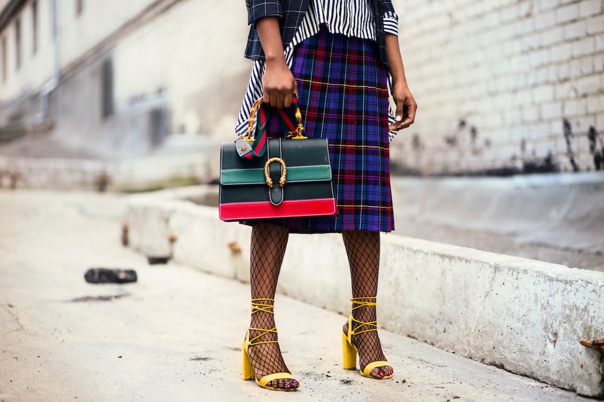 Mulher com uma bolsa verde e vermelha parada com roupa estilosa