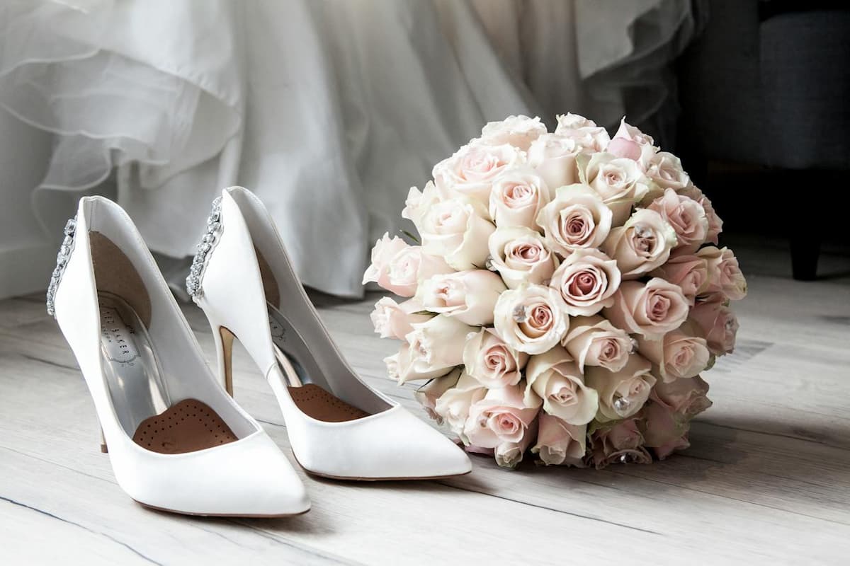 Imagem de um buquê de rosas com um salto branco no chão|Imagem de um brinde com os convidados|Imagem de uma noiva com suas madrinhas com vestido rosa|Imagem de uma mesa de lembrancinhas|Noivos se beijando enquanto os convidados comemoram|Mulher de vestido de noiva segurando buquê de rosas|Imagem de decoração de estrelas do mar em casamento|Mesa de casamento com decorações de flores e um bolo|Imagem de um convite de casamento|Mulher com vestido de noiva segurando um buquê|Imagem de uma mesa de casamento com decoração branca