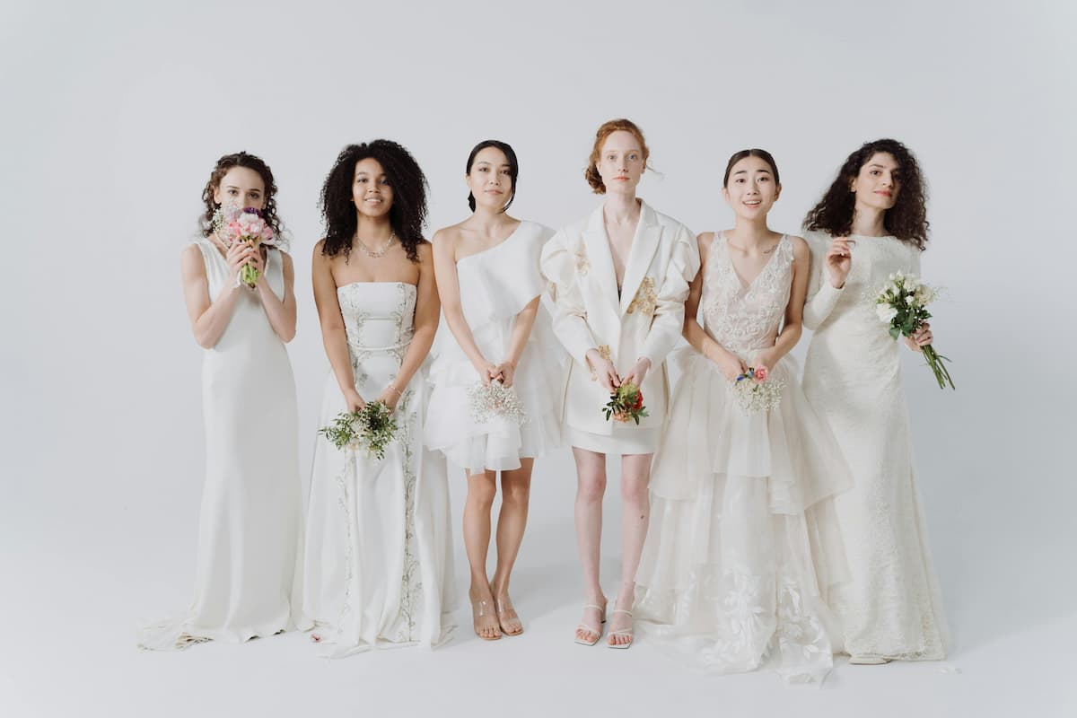 6 mulheres com diferentes estilos de vestido de noiva|Noiva com vestido estilo princesa.|Noiva com vestido curto.|Noiva com vestido estilo natural.|Vestido de noiva com corsete à mostra.|Noiva com vestido de gola alta.|Noiva com vestido tomara que caia.|Noiva com decote quadrado.||Noiva caminha por um gramado de costas para o pôr do sol.||Uma mulher com um vestido de noiva estilo sereia|Uma noiva usando um vestido Corte Évasé e ao fundo um lago|Uma noiva segurando seu buquê e um vestido com corte império|Uma noiva apoiada com o braço em um tronco de árvore com o vestido estilo brigerton|Uma noiva se olhando pelo espelho|Uma noiva segurando seu buquê e com um vestido de renda personalizado|Uma noiva mexendo em seu coque